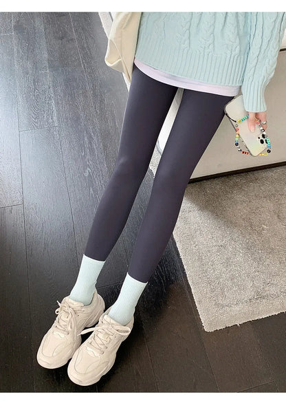 Person wearing dark gray leggings, light blue sweater, and white sneakers on a wooden floor.