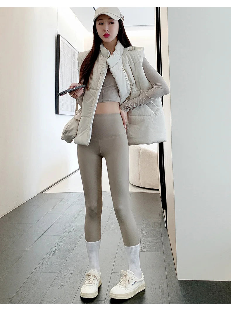 Woman in a stylish outfit with a puffer vest and leggings standing in a modern interior setting.