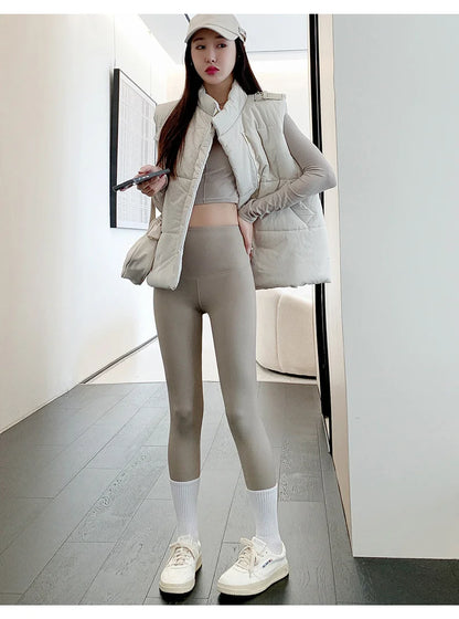 Woman in a stylish outfit with a puffer vest and leggings standing in a modern interior setting.