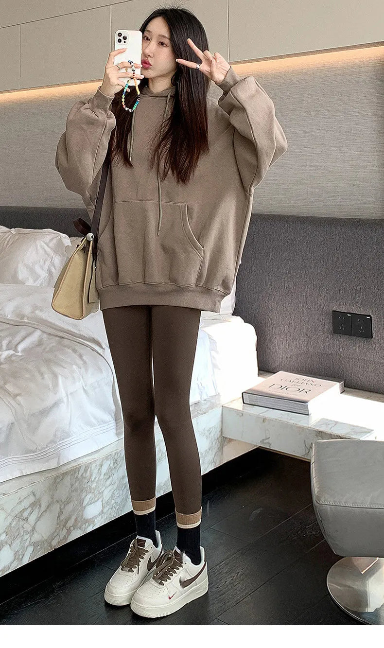 Woman taking a mirror selfie wearing a beige hoodie and leggings in a bedroom.