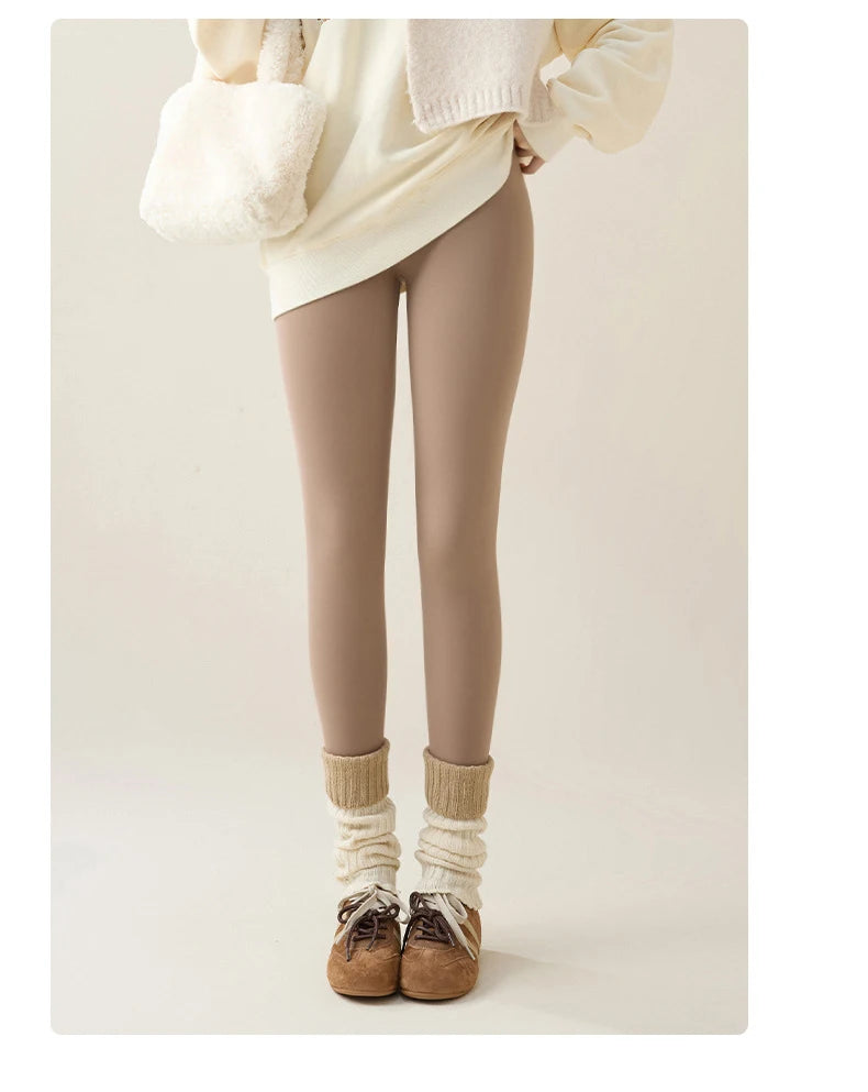 Person wearing beige leggings, white sweater, and brown shoes on a plain background