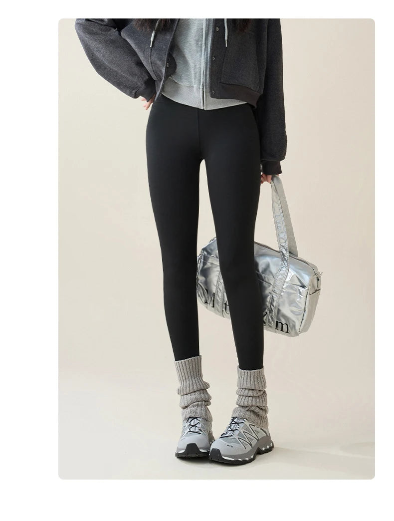 Person wearing black leggings, gray sneakers, and a dark jacket with a light background