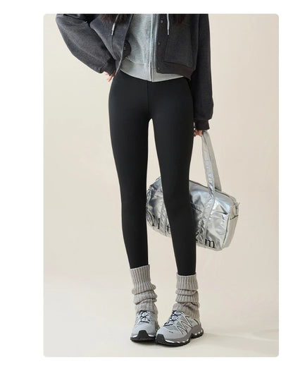 Person wearing black leggings, gray sneakers, and a dark jacket with a light background