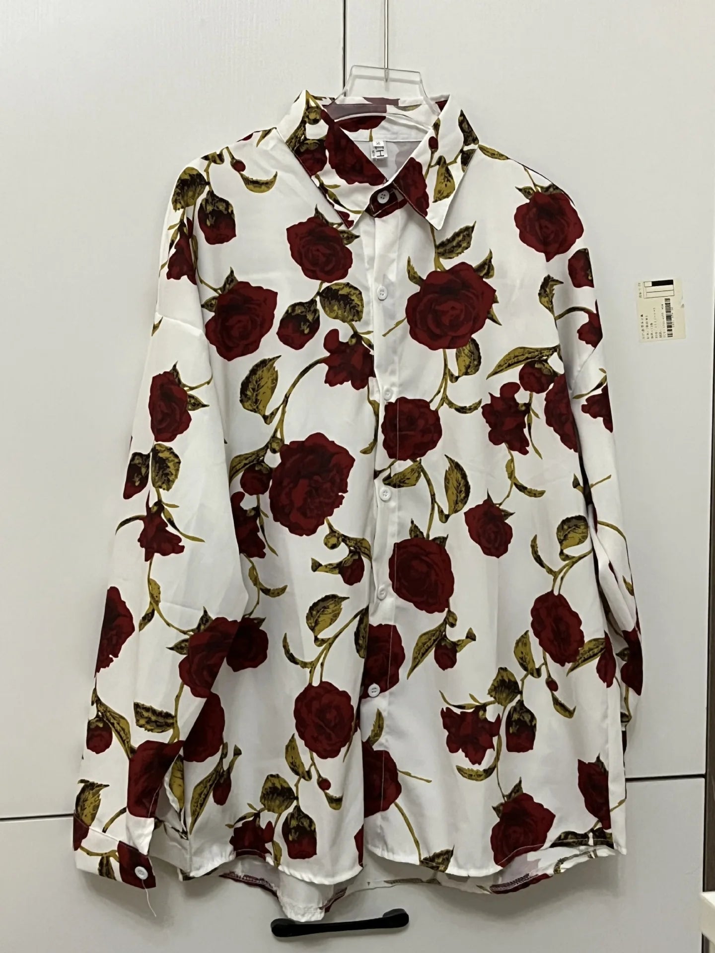Floral blouse with red roses on a hanger against a white wall