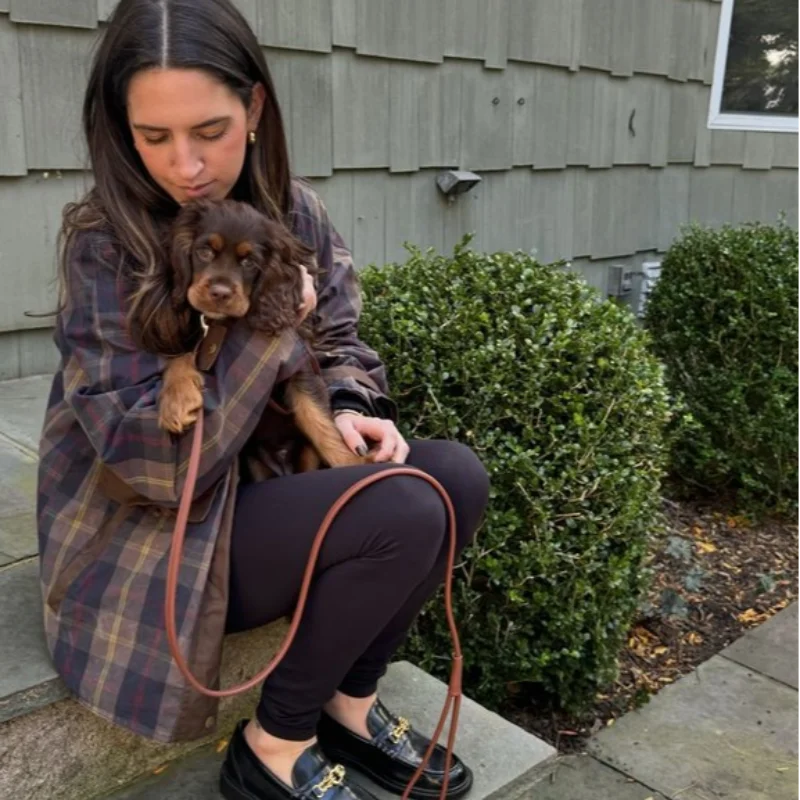 Woman holding a small dog outdoors in front of a house.