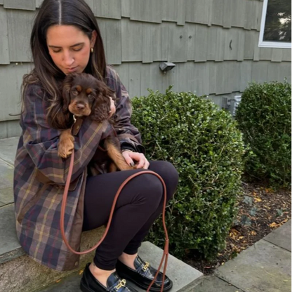 Woman holding a small dog outdoors in front of a house.
