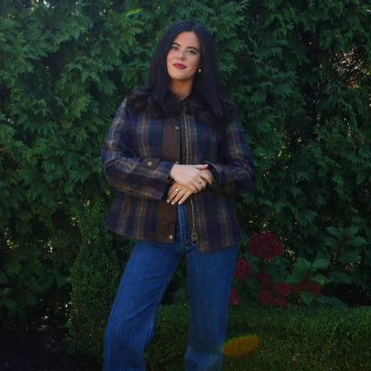 Woman wearing a plaid jacket and blue jeans standing in front of green bushes