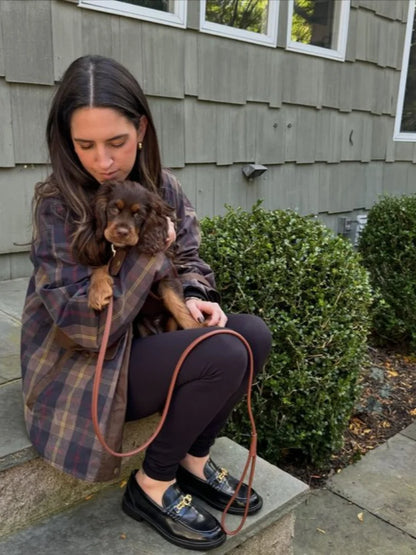 Woman holding a small dog wrapped in a plaid blanket outdoors.