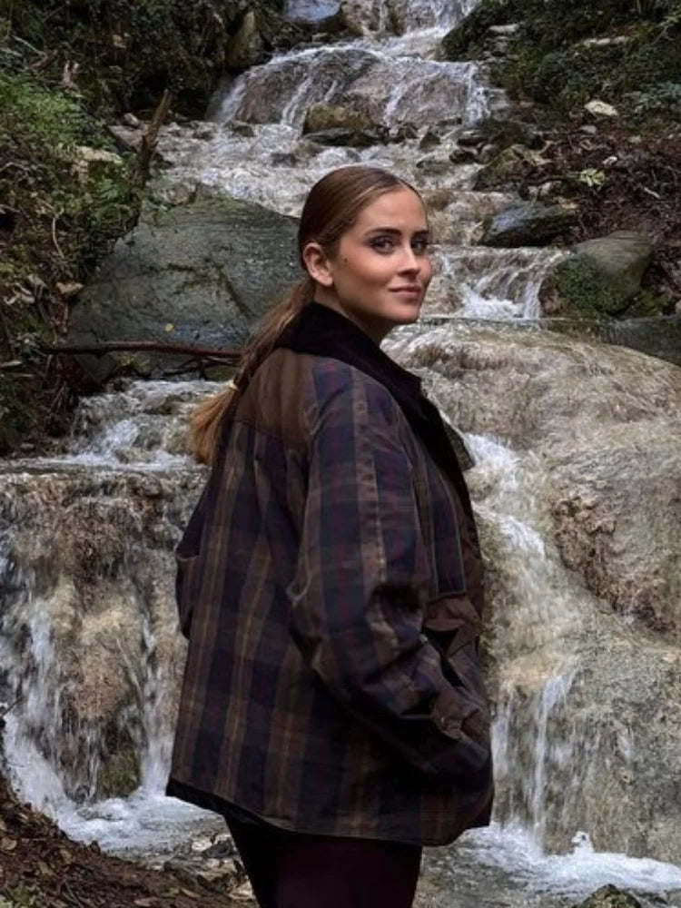 Woman standing in front of a waterfall wearing a plaid jacket.