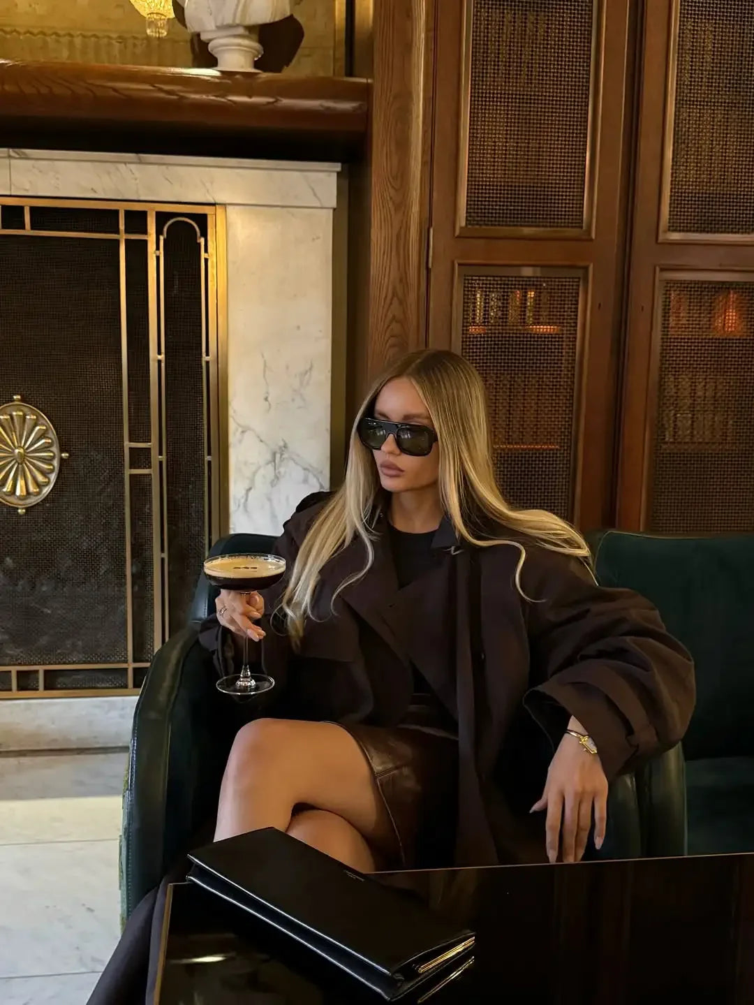 Woman in a stylish outfit holding a drink in an elegant interior setting