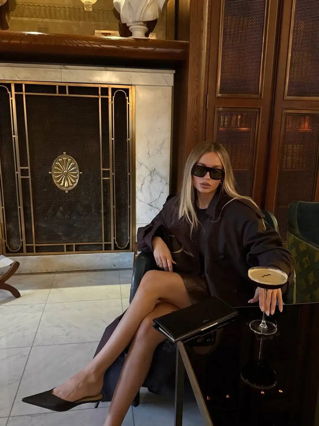 Woman in a black outfit sitting in a stylish interior setting with a fireplace.