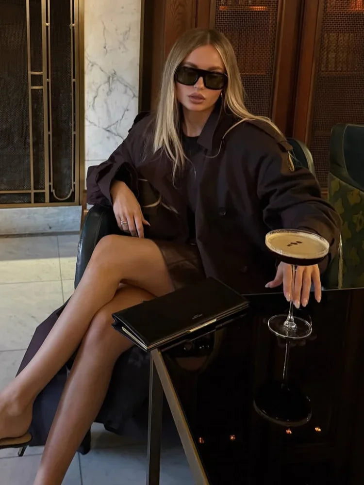 Woman in a black outfit sitting at a table with a drink, wearing sunglasses.