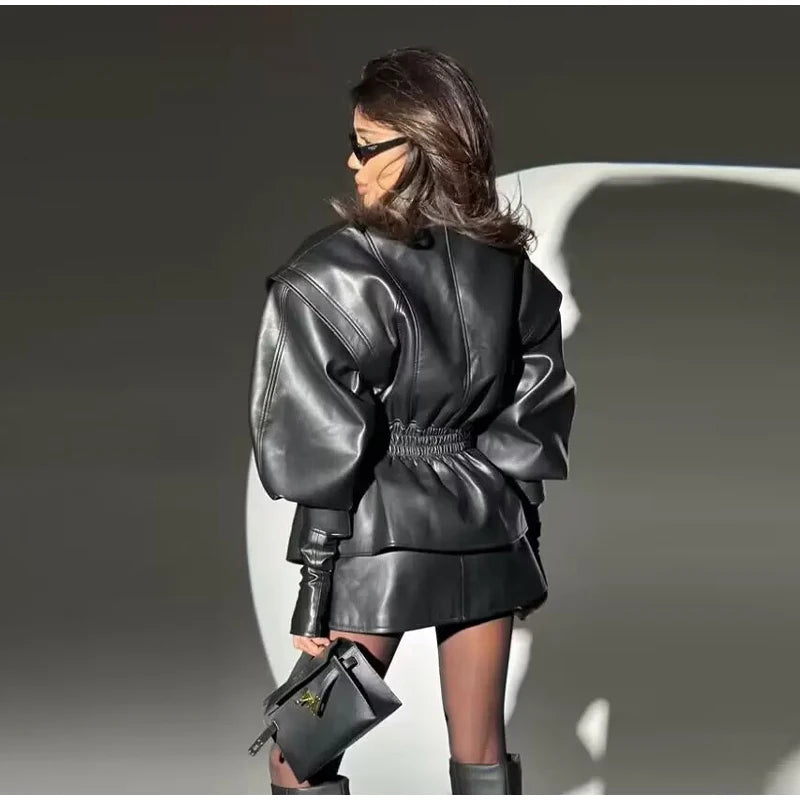 Person wearing a black leather outfit with sunglasses against a neutral background