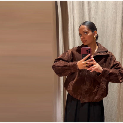 Person wearing a brown jacket taking a mirror selfie against a neutral background