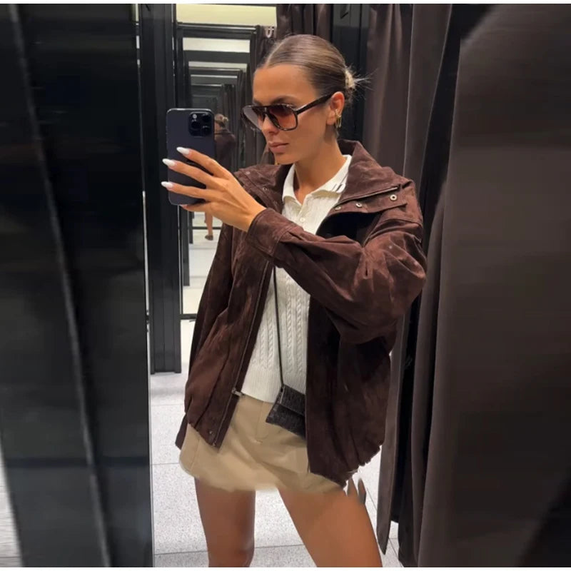 Woman taking a mirror selfie wearing a brown jacket and sunglasses.