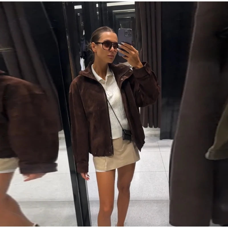 Woman taking a mirror selfie wearing a brown jacket and white shirt.