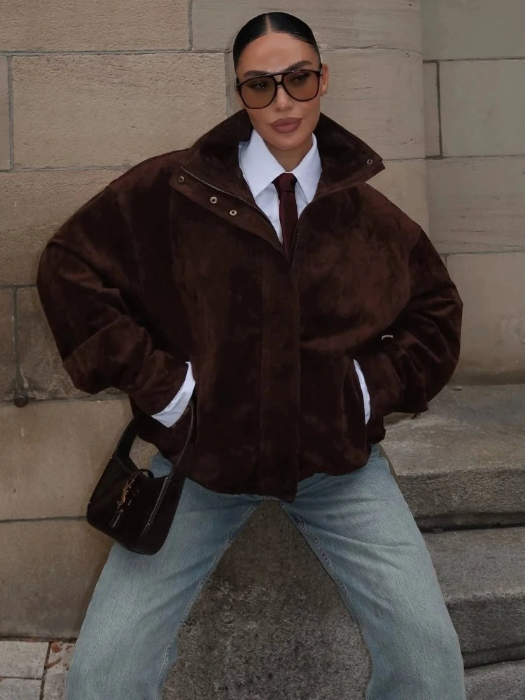 Person wearing a brown fur coat and sunglasses against a stone wall.
