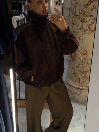 Person wearing a brown turtleneck sweater and beige pants taking a mirror selfie.