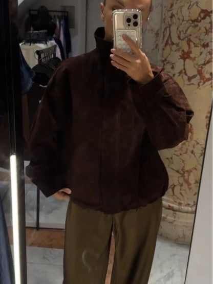 Person wearing a brown jacket and green pants in front of a mirror.