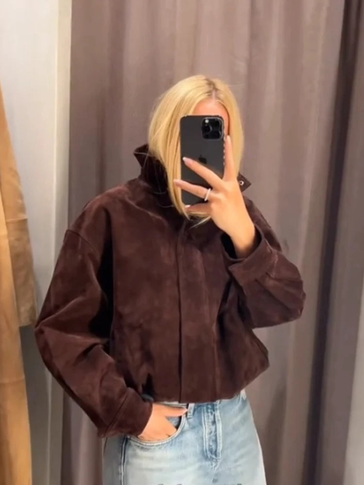 Person wearing a brown jacket and light blue jeans taking a mirror selfie.