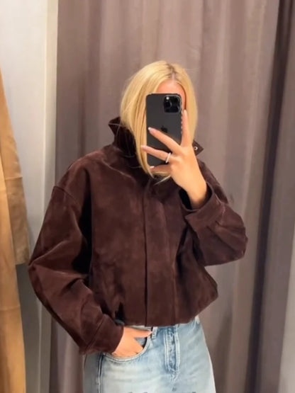 Person wearing a brown jacket and light blue jeans taking a mirror selfie.