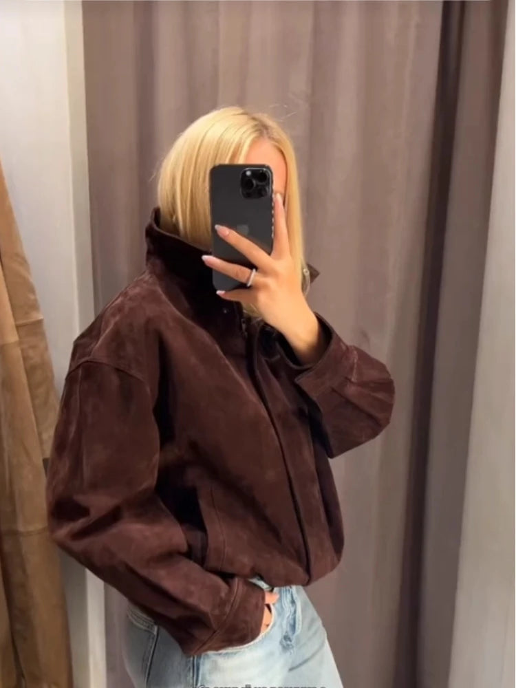 Person wearing a brown jacket in front of a neutral curtain