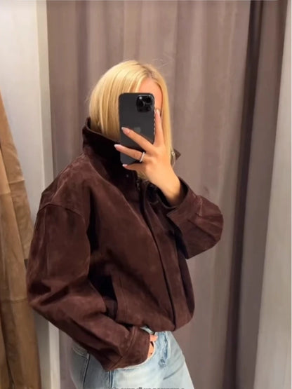 Person wearing a brown jacket in front of a neutral curtain