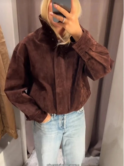 Person wearing a brown jacket and light blue jeans in front of a mirror.