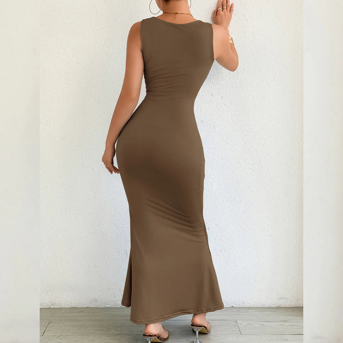 Woman wearing a brown sleeveless dress against a white wall.