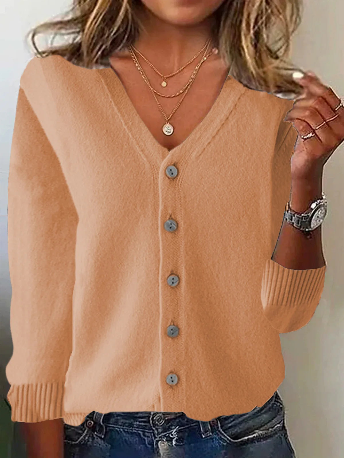 Person wearing a beige cardigan with buttons, layered necklaces, and a watch.