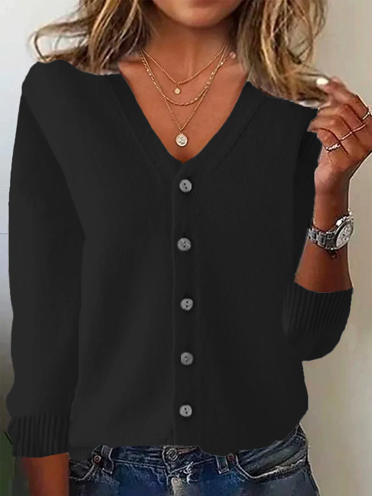 Person wearing a black cardigan with layered necklaces and a watch.