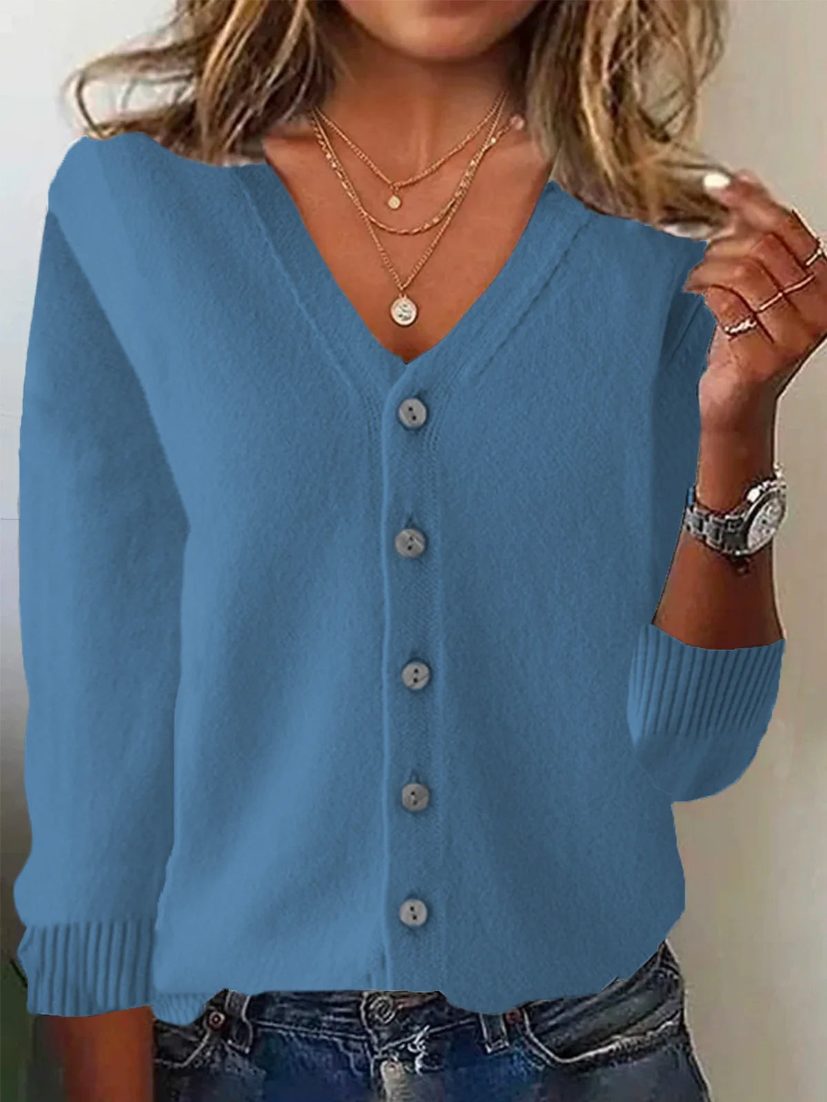 Blue cardigan worn by a person with layered necklaces and a watch.