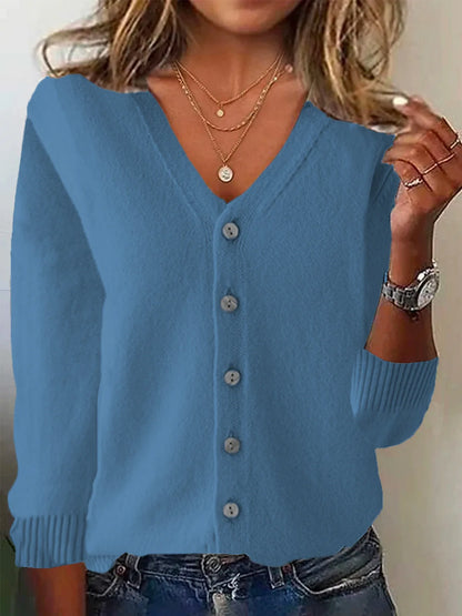 Blue cardigan worn by a person with layered necklaces and a watch.