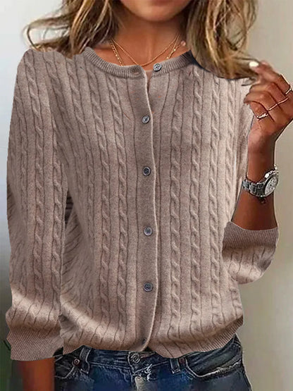 Person wearing a beige cable knit cardigan with a neutral background