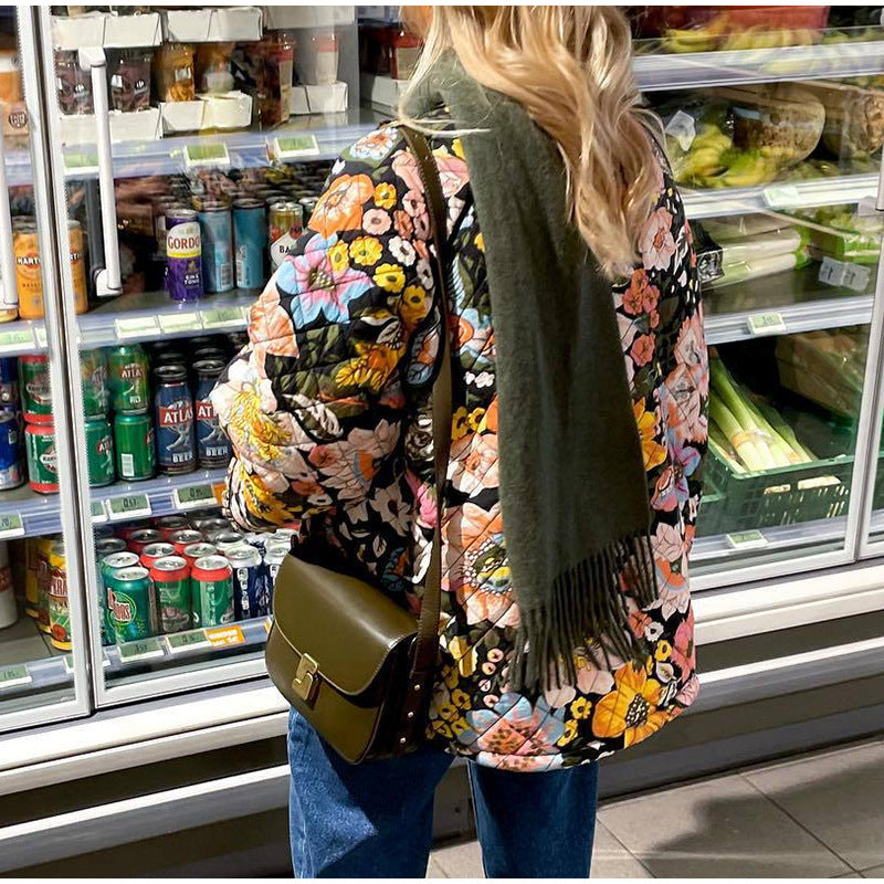Person wearing a floral coat and green scarf in a grocery store aisle.