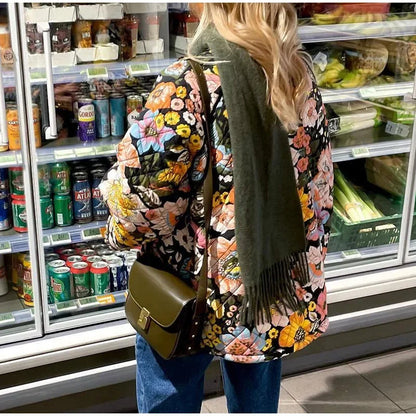 Person wearing a floral coat and green scarf in a grocery store aisle.