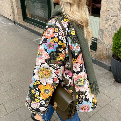 Person wearing a colorful floral jacket with a green bag on a sidewalk.