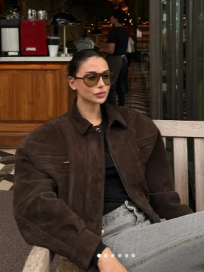Person wearing a brown jacket and sunglasses sitting on a bench in an outdoor setting.