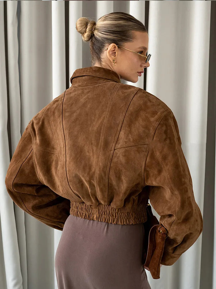 Woman wearing a brown suede jacket in front of white curtains