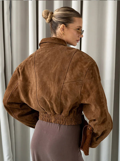 Woman wearing a brown suede jacket in front of white curtains