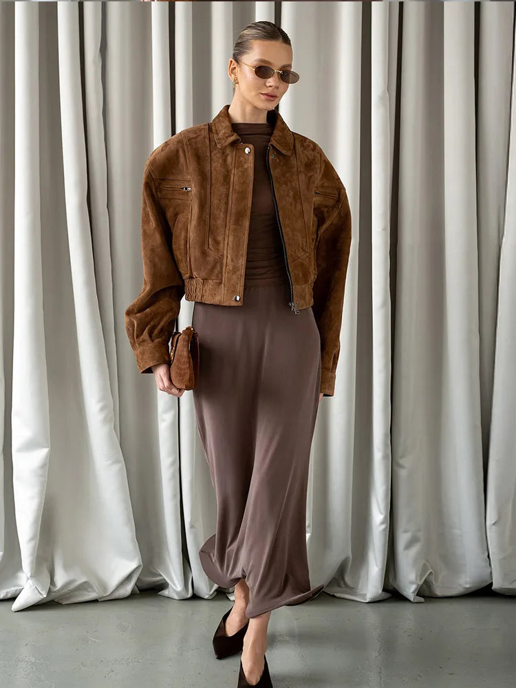 Woman wearing a brown jacket and skirt standing in front of white curtains.