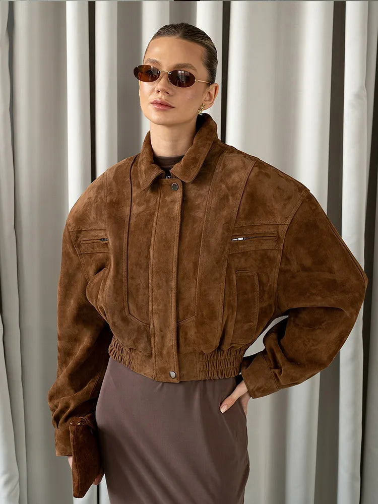 Person wearing a brown suede jacket and sunglasses against a neutral background