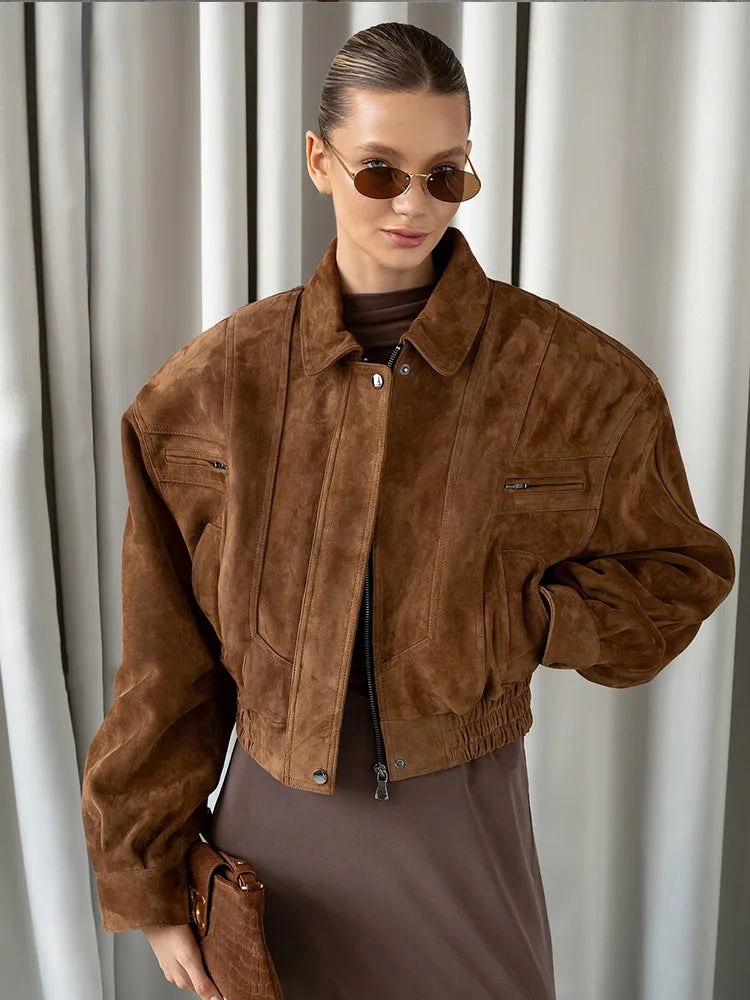 Person wearing a brown suede jacket and sunglasses against a neutral background
