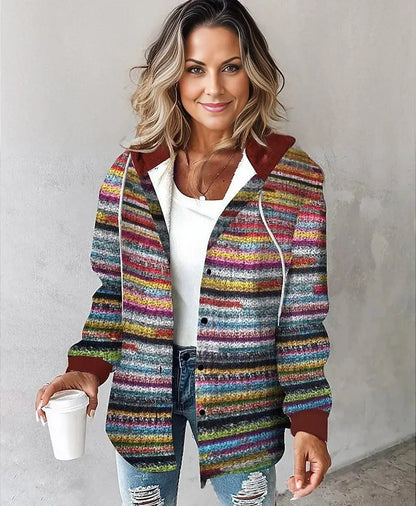 Woman wearing a colorful striped jacket holding a white cup against a plain background