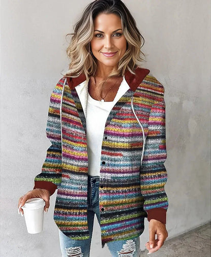 Woman wearing a colorful striped jacket holding a white cup against a plain background