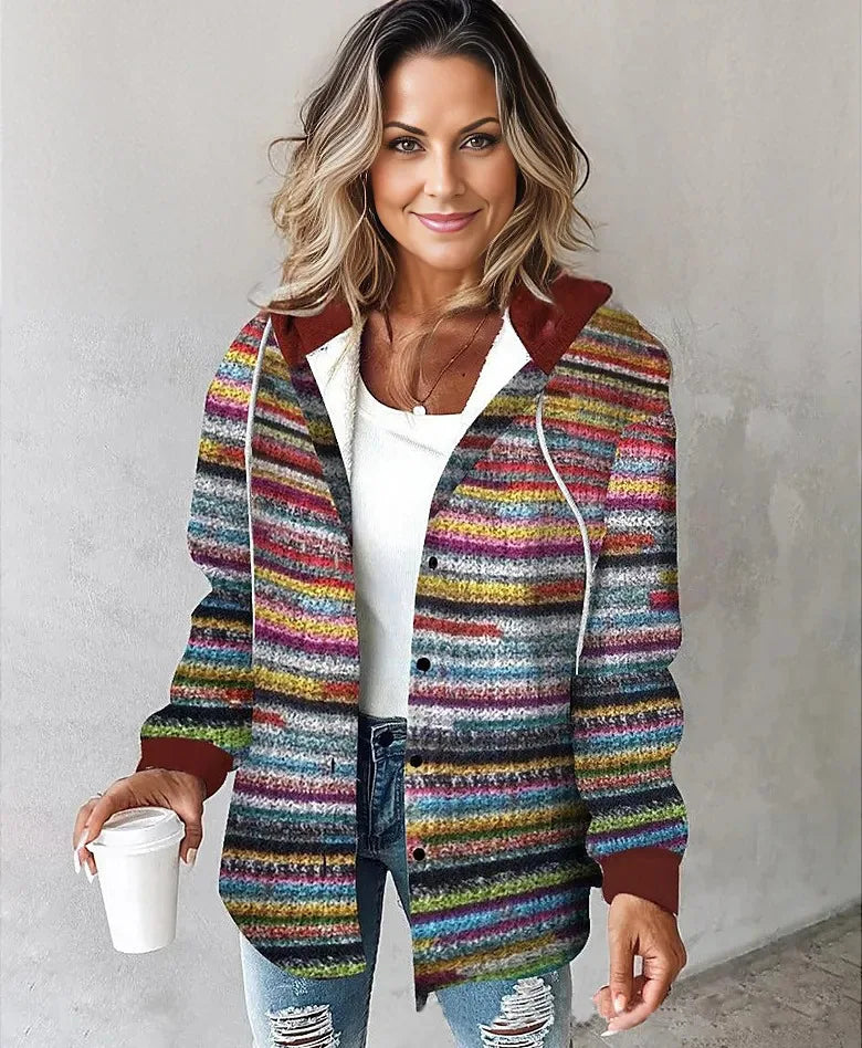 Woman wearing a colorful striped jacket holding a white cup against a plain background