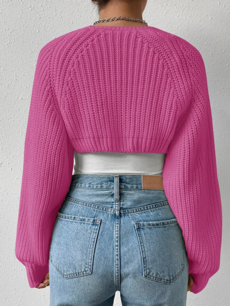 Person wearing a bright pink knitted sweater and blue jeans against a plain background