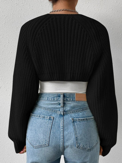 Person wearing a black ribbed sweater and blue jeans with a white belt.