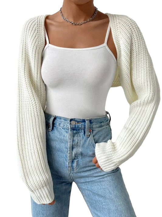Person wearing a white knit cardigan over a white tank top and blue jeans on a white background