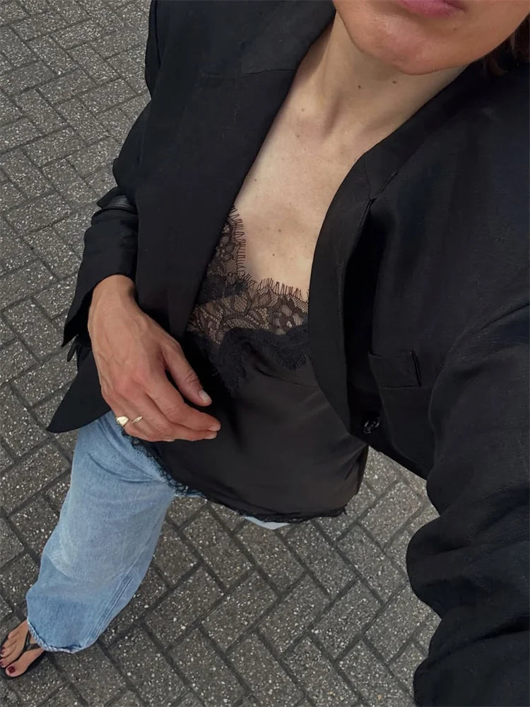 Person wearing a black jacket with a lace top underneath on a paved ground.